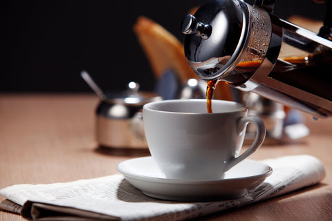 French press pouring coffee into a white cup